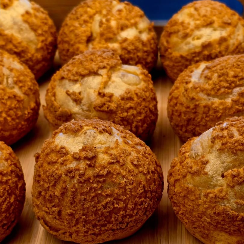 Close-up of golden-brown choux pastries with a textured, crispy topping on a wooden surface.