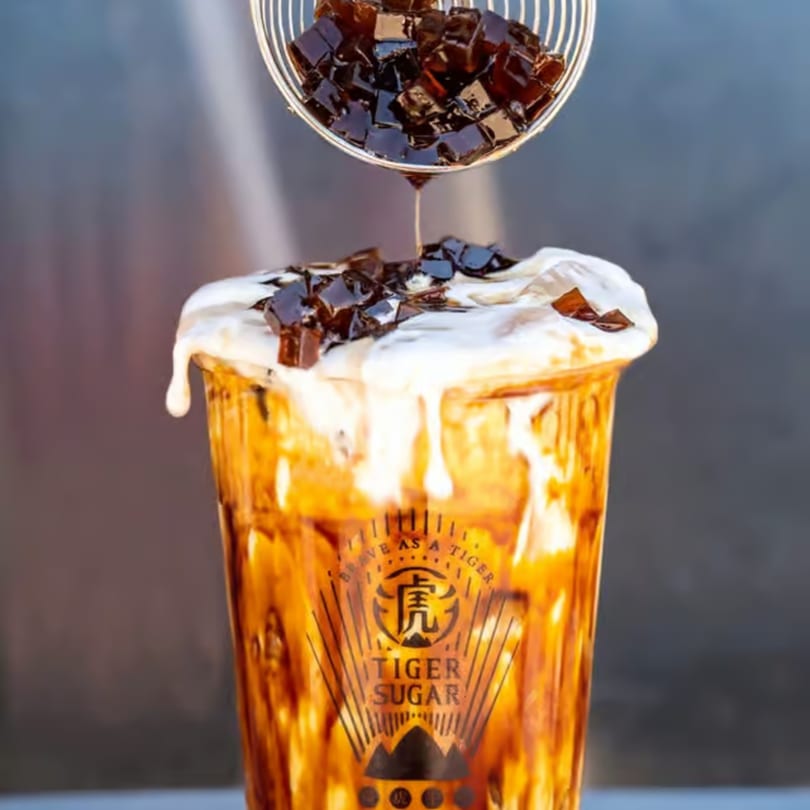 Tiger Sugar boba drink with cream foam and brown sugar jelly cubes being poured on top.