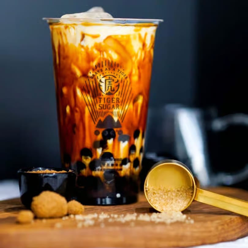 Tiger Sugar brown sugar boba drink with cream, next to brown sugar in a scoop and bowl.