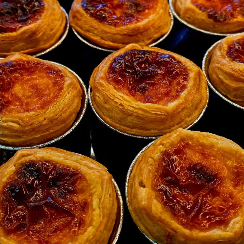 Close-up of several golden-brown Portuguese custard tarts (Pastéis de Nata) in foil cups.