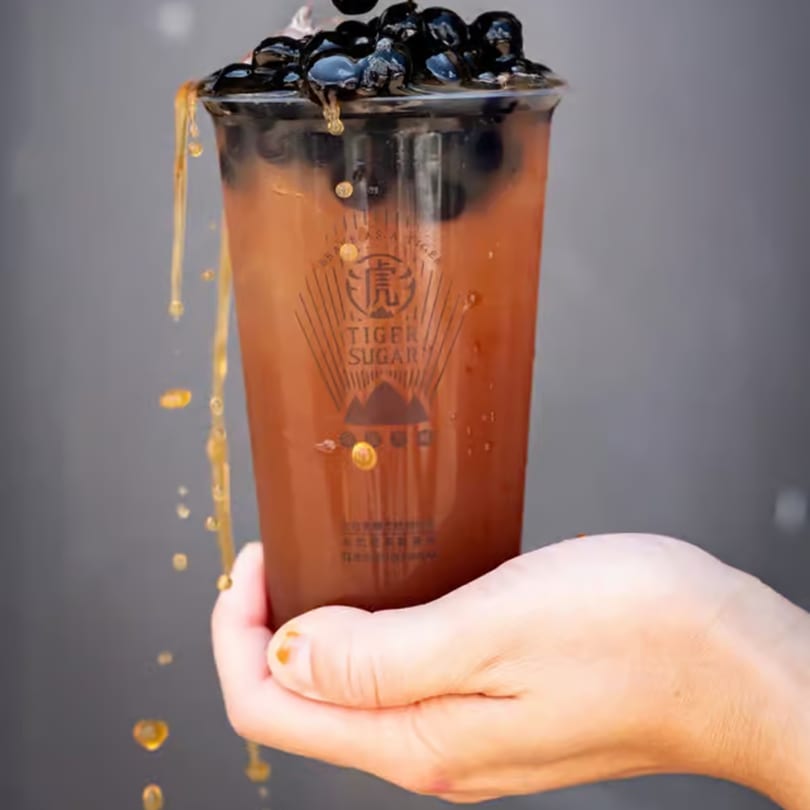 Hand holding a Tiger Sugar bubble tea with brown sugar syrup dripping down the side.